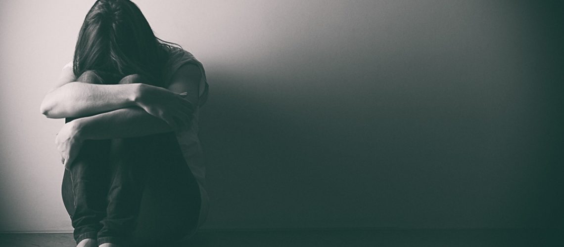 Teenager girl with depression sitting alone on the floor in the dark room. . Black and white photo