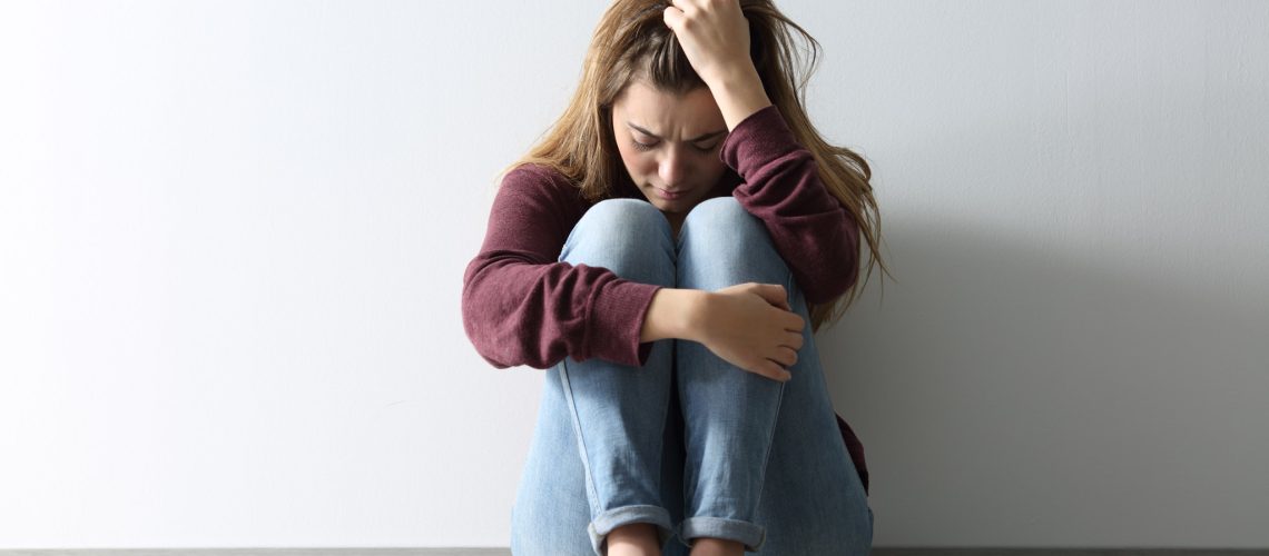 Front view full body portrait of a sad woman sitting on the floor at home
