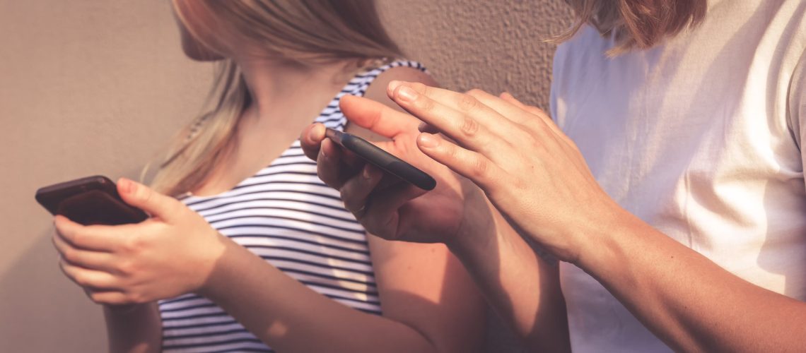 Group of multicultural friends using a smartphone outdoors. Hands of people dependent on a mobile smartphone. Teenager generation z lifestyle, hobbies, digital addiction.