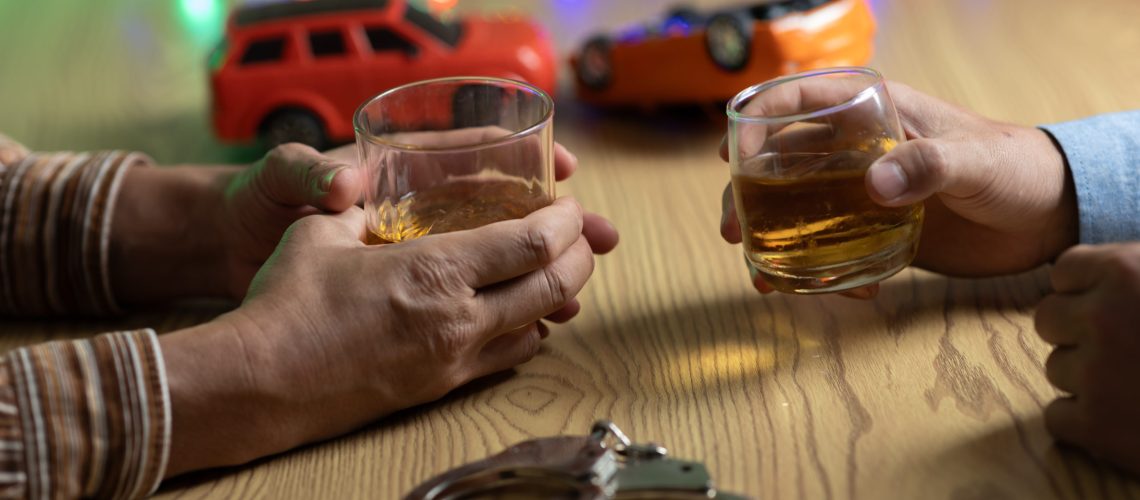 Two men clink whiskey glasses while in front of a bar in a restaurant. With a small car model on the table. The concept of drunk driving is to avoid the risk of accidents.
