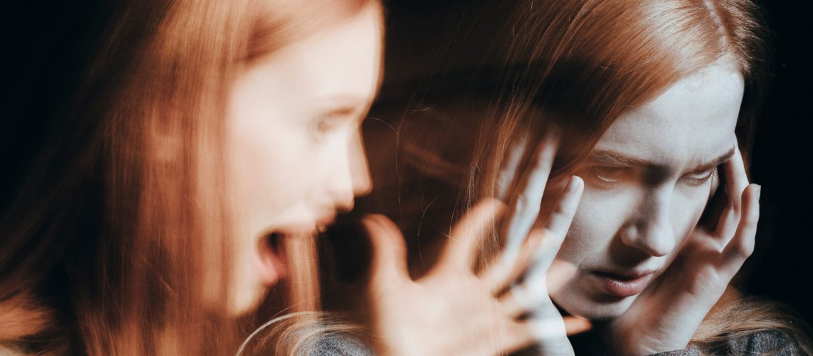 Girl with schizophrenia covering her ears to not hear the voice of alter ego. Blurred person