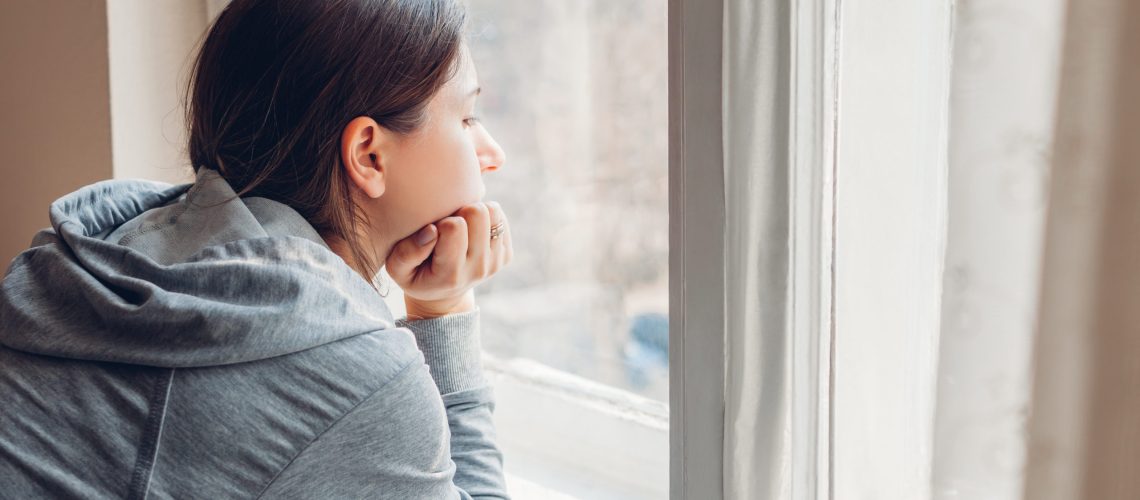 Isolation at home during coronavirus covid-19 pandemic. Woman looking at window. Sad girl stays safe at home on quarantine