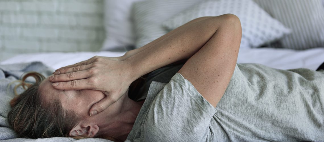 Desperate lady is closing her face in own hands. She lying on bed