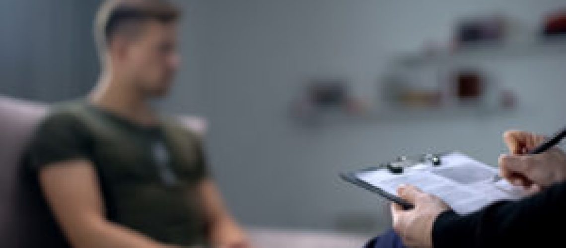 Psychologist making notes during therapy session with sad male soldier, PTSD