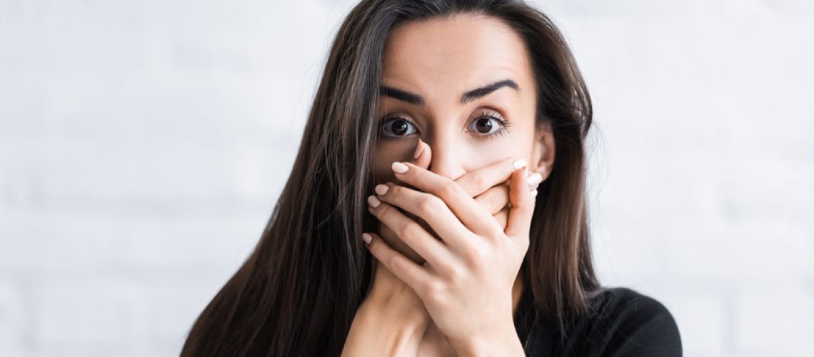 frightened young man looking at camera and covering face with hands while suffering from panic attack