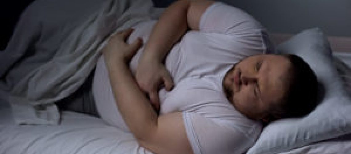 Fat man suffering from stomach pain at night, health problem, ulcer discomfort