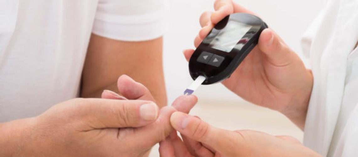 Close-up Of Doctor's Hand Using Glucometer On Patient's Finger