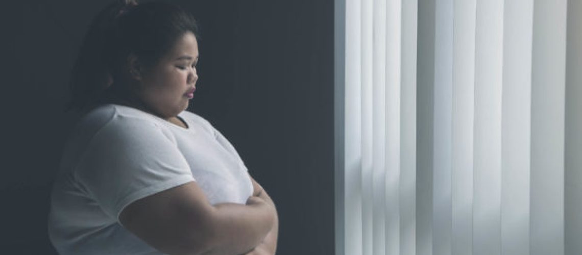 Picture of lonely obese woman looks sad while standing near the window