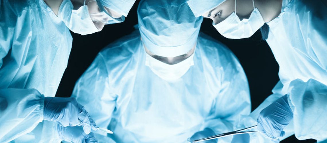 41331167 - medical team performing operation. group of surgeon at work in operating theatre tonned in blue