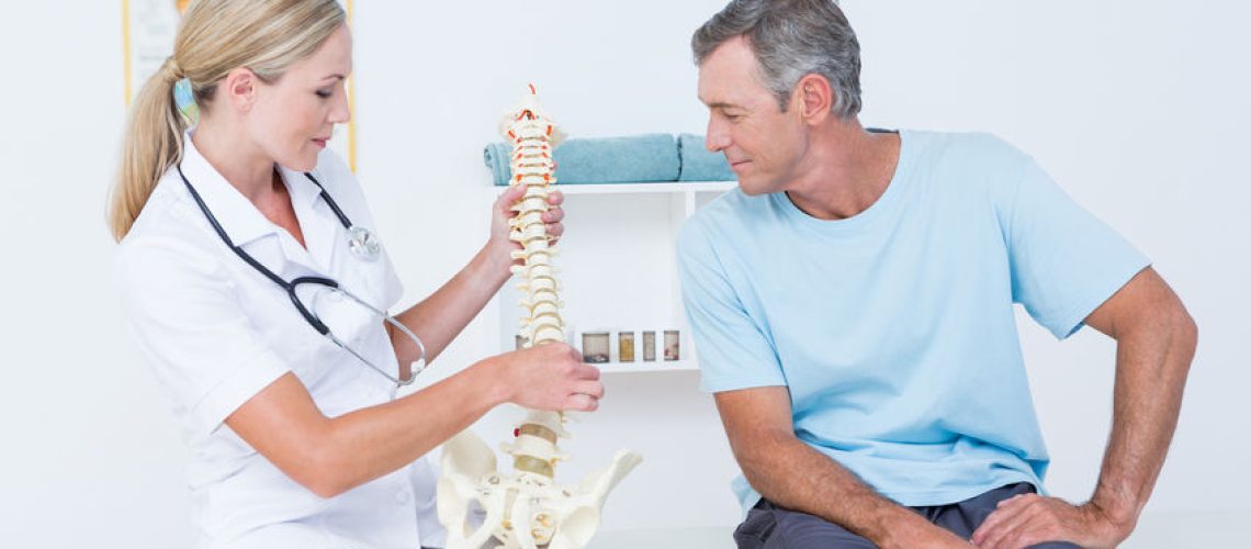 Doctor showing anatomical spine to her patient in medical office